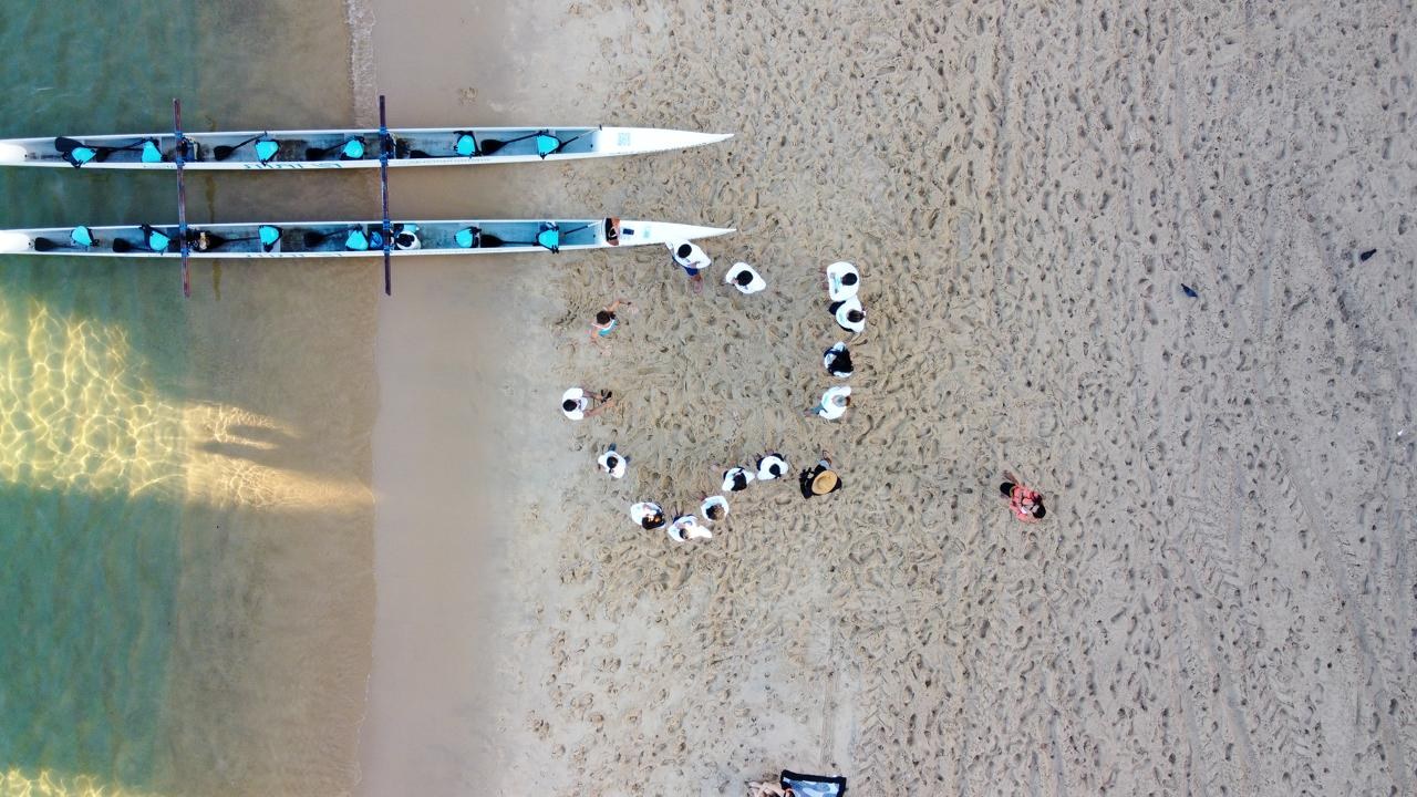 Vista aérea de participantes e canoas na praia